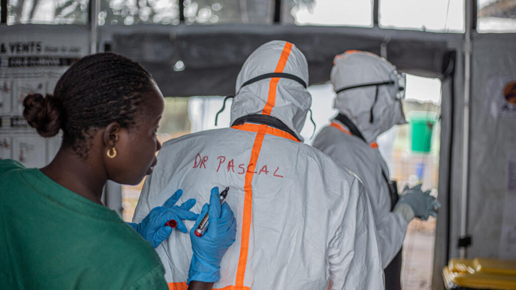 Un agent d'hygiène inscrit le nom d'un médecin au dos de sa combinaison de protection individuelle (EPI) avant d'entrer dans le centre de traitement Ebola (CTE) de Rwampara pour soigner des patients atteints de la maladie à virus Ebola, à Bunia (Ituri), dans l'est de la république Démocratique du Congo, le 13 juillet 2026.